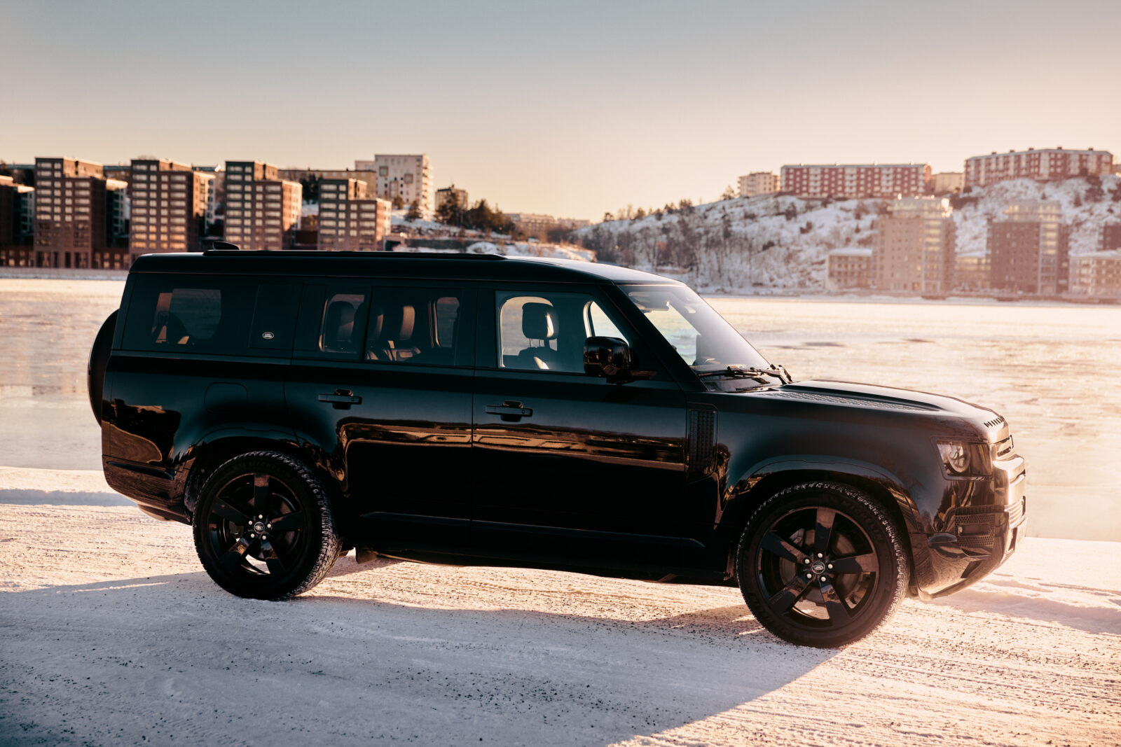 Svart SUV på frusen sjö med stadssilhuett i bakgrunden.